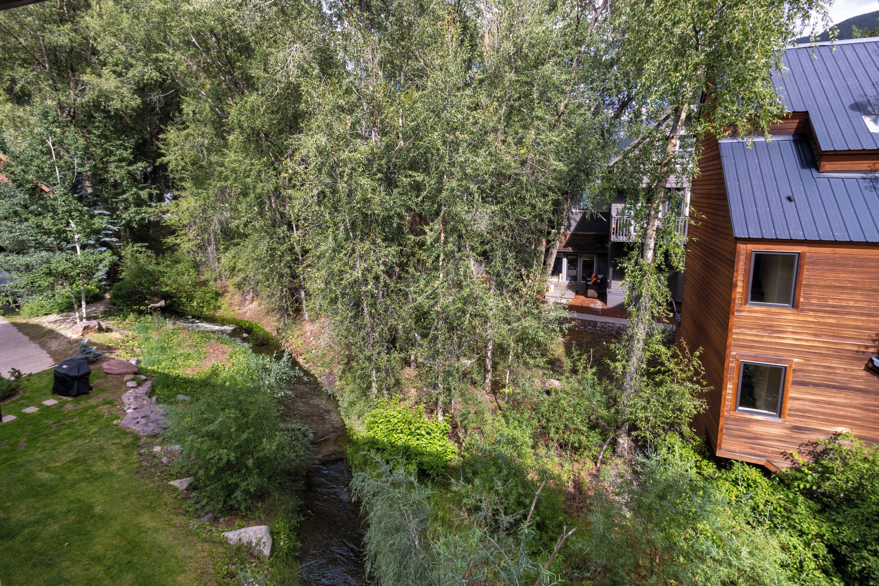 A modern two-story building with a sloped roof, surrounded by dense greenery and a small stream.