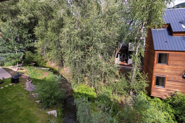 Un bâtiment moderne à deux étages, doté d’un toit en pente, entouré d’une végétation luxuriante et traversé par un petit ruisseau.