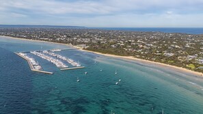 An aerial view of a coastal marina with boats docked, a sandy beach, and a residential area in the background. - Koonya Blairgowrie Luxe Retreat | Pet Friendly, Walk to Beach (Blairgowrie)