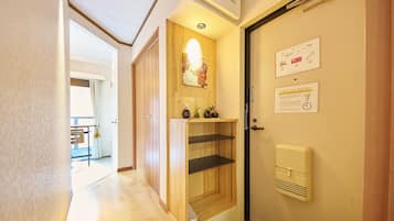 A hotel hallway with a wooden door, a small shelf with decorative items, and a wall-mounted air conditioning unit.