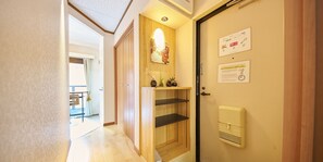 A hotel hallway with a wooden door, a small shelf with decorative items, and a wall-mounted air conditioning unit. - DIA PALACE OHTEMON (Kanazawa)