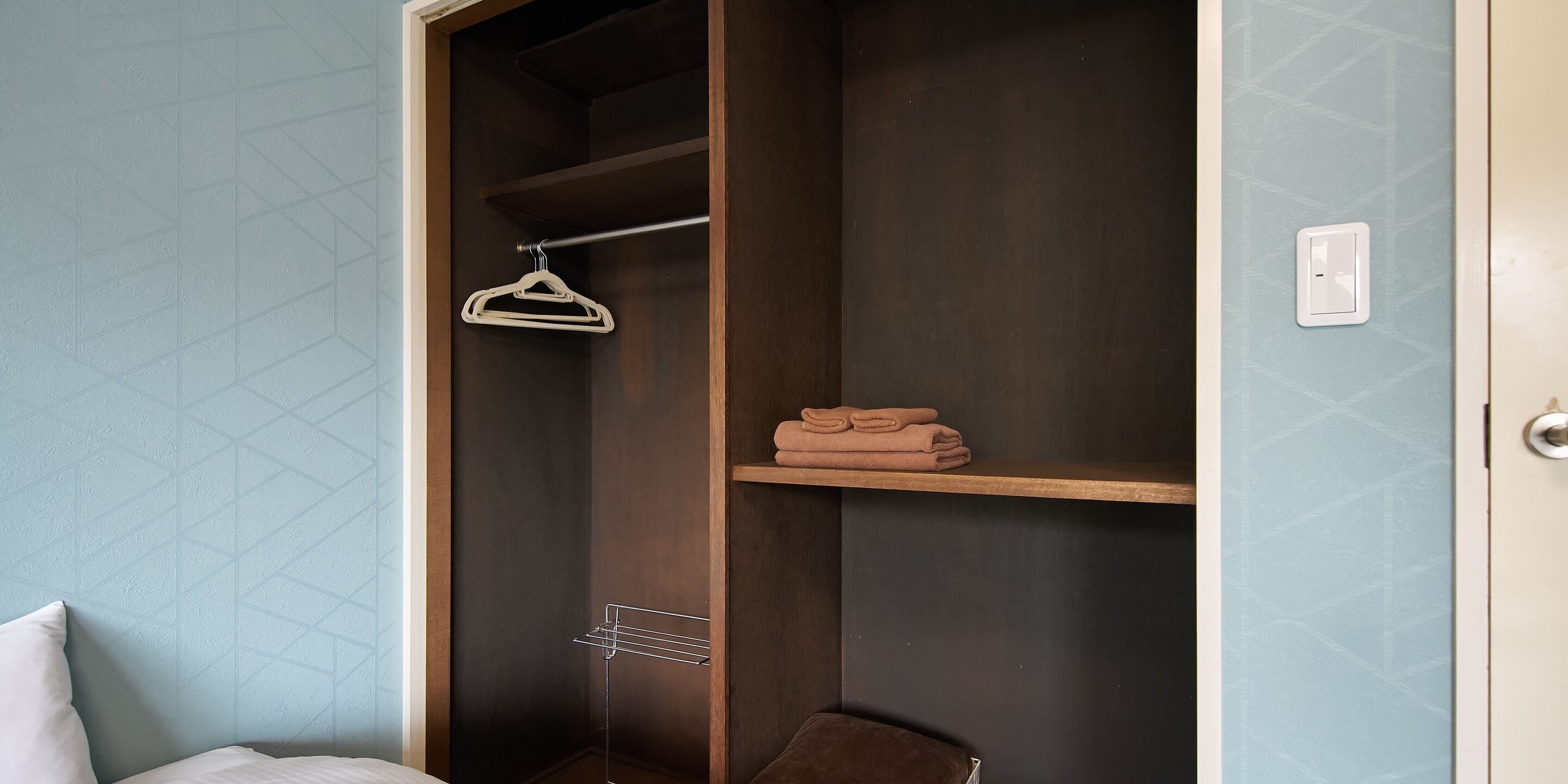 A room with a wardrobe, a hanging rack, and a shelf with folded towels.