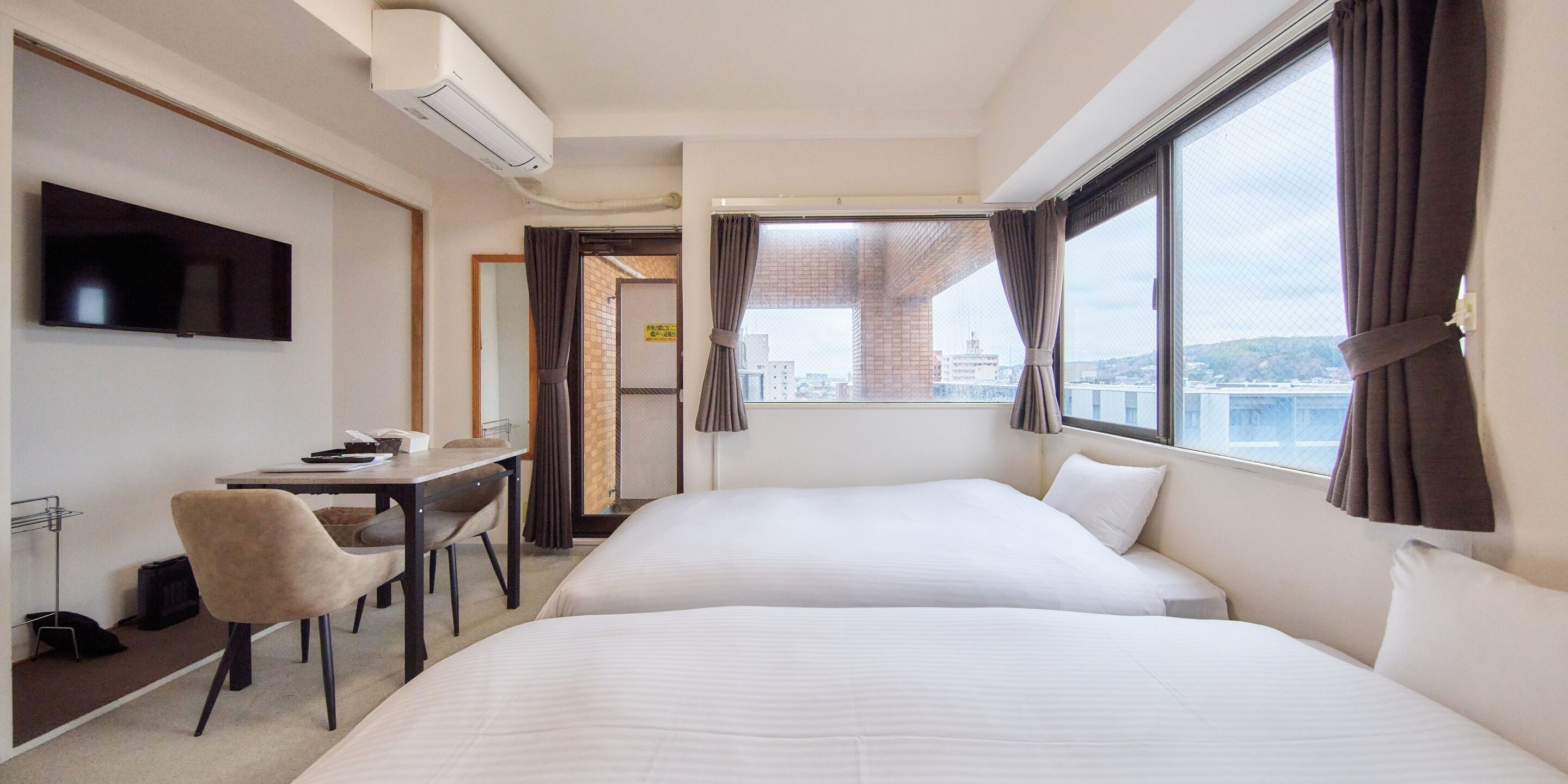 A hotel room with two beds, a desk, a chair, a television, and a window with curtains.