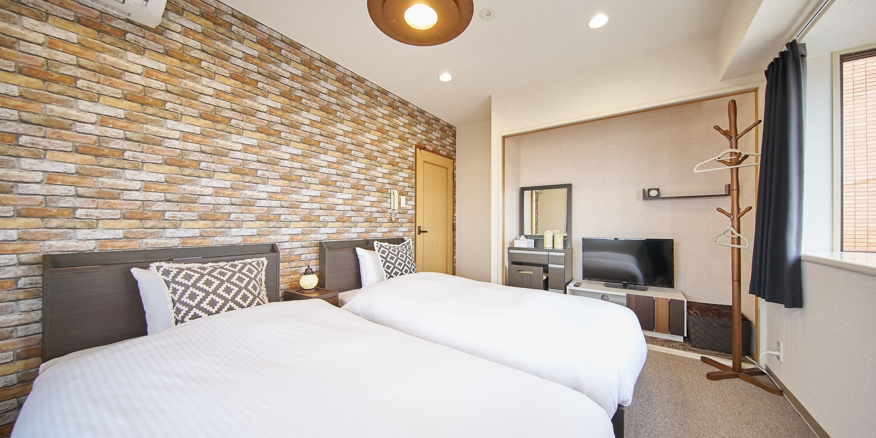 Een hotelkamer met een bakstenen muur, een bed met witte lakens, een televisie en een spiegel.