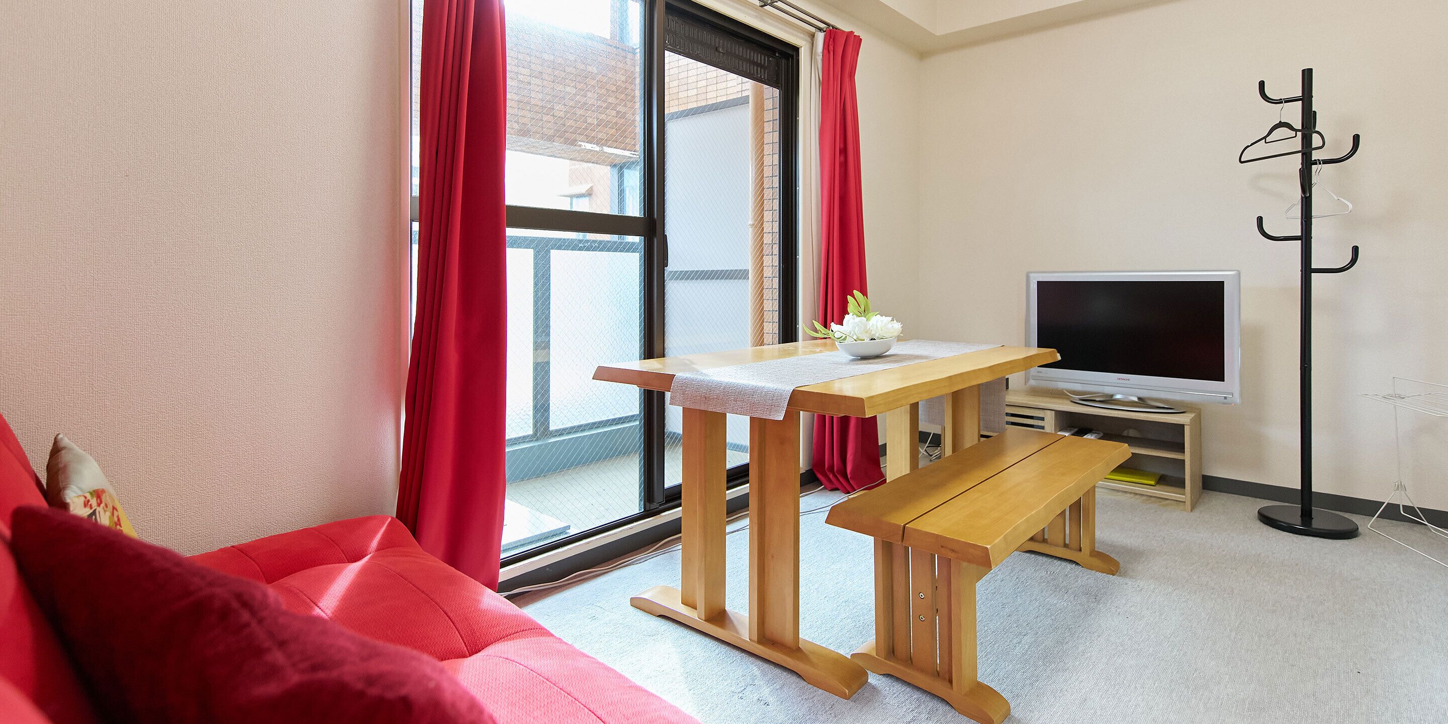 Una habitación con un sofá, una mesa con un florero, un banco, un perchero y un televisor.