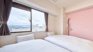 Een hotelkamer met twee bedden, een raam met gordijnen, een kapstok en uitzicht op de stad.