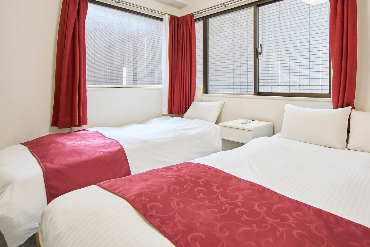 Habitació d'hotel amb dos llits, una tauleta de nit i una finestra amb persianes.