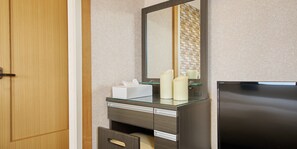 Quarto de hotel com porta de madeira, espelho, minibar e geladeira preta.