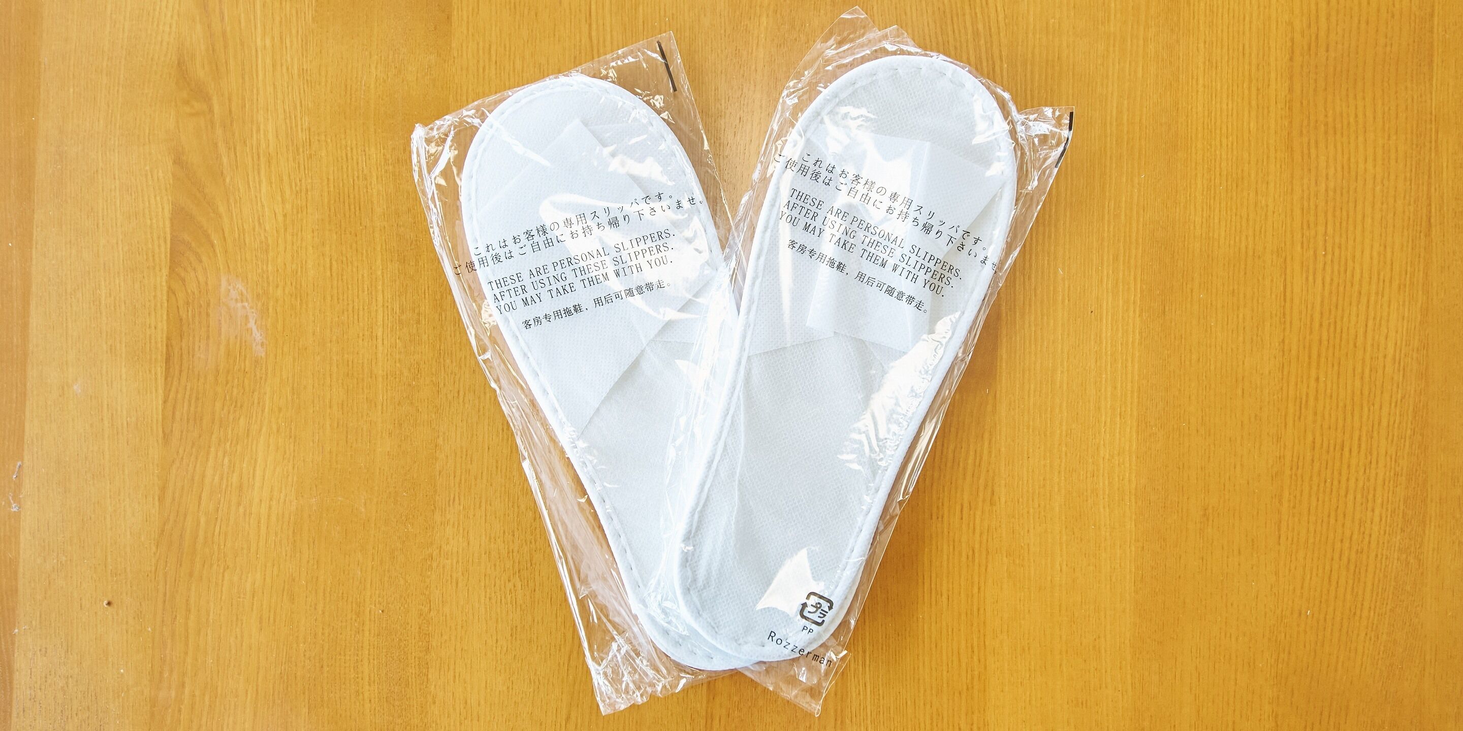 A pair of slippers in plastic packaging on a wooden surface.