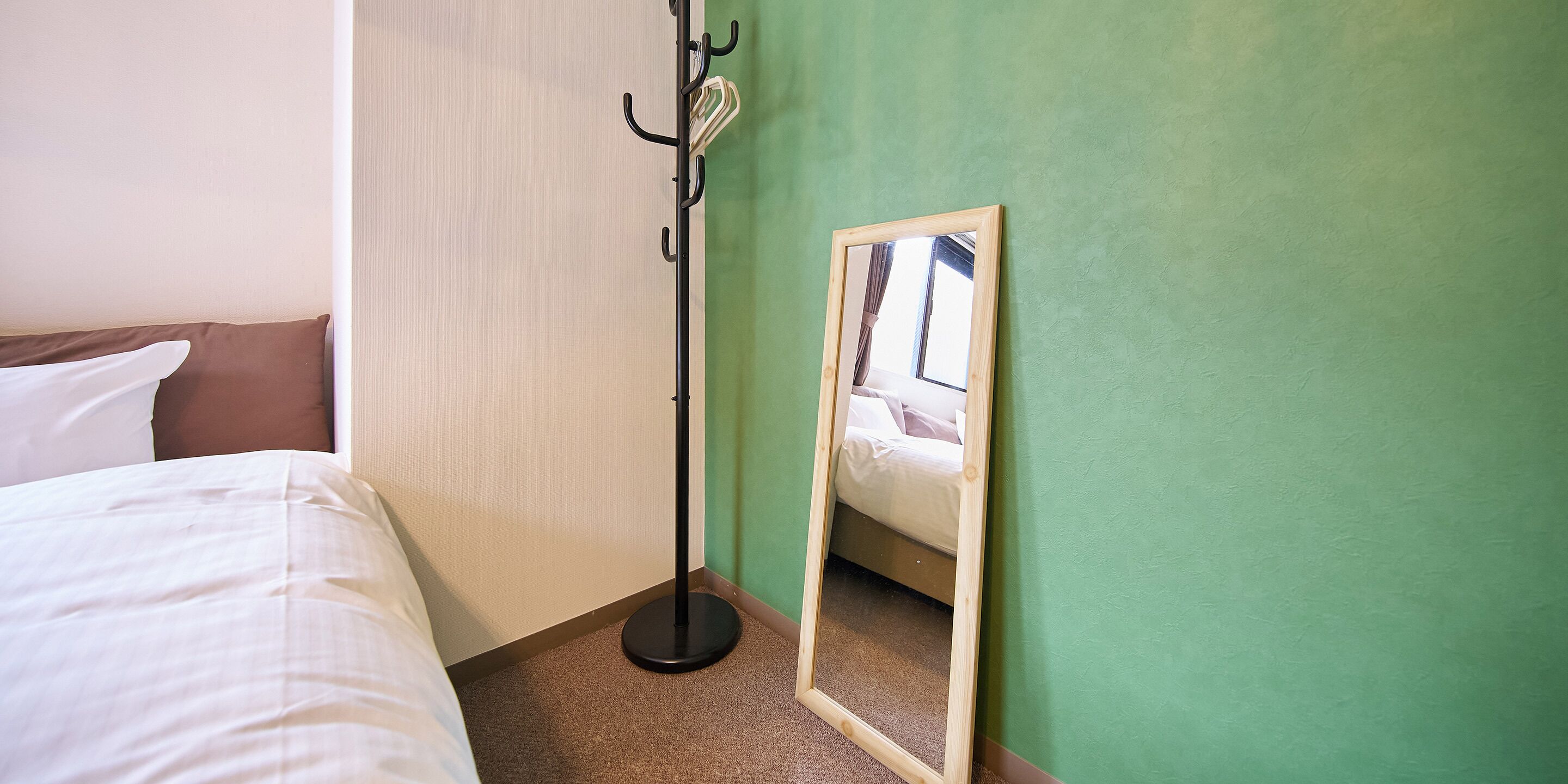 Une chambre d’hôtel avec un lit, un porte-manteau et un miroir qui reflète la pièce.