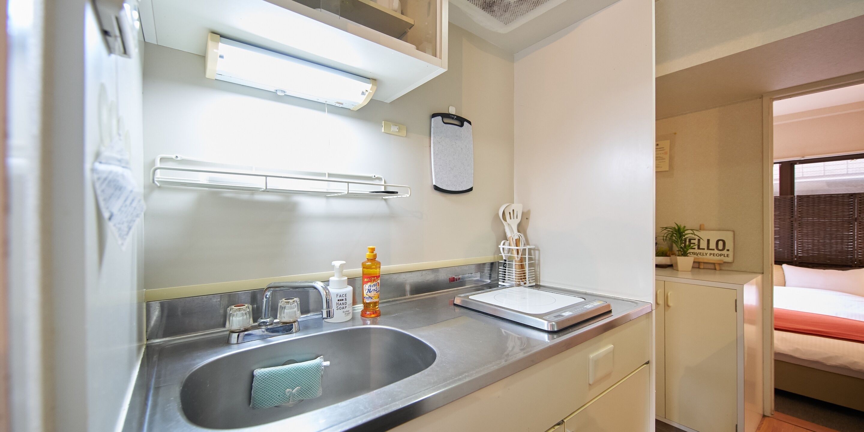 A modern bathroom with a stainless steel sink, a mirror, a towel rack, and a soap dispenser.