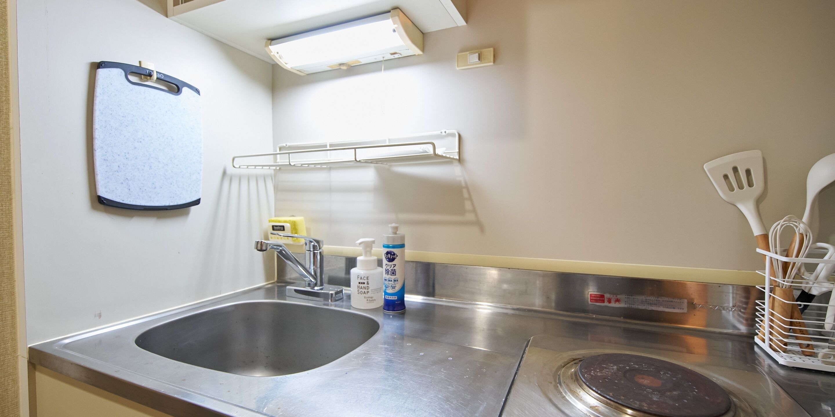 Una cocina con un lavamanos de acero inoxidable, un grifo, dispensador de jabón y un portalápices para espátulas.