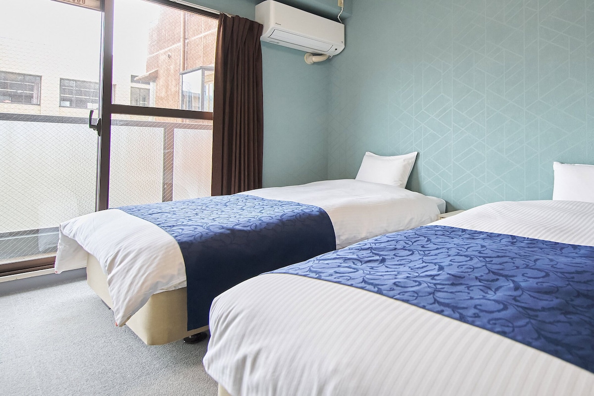 Habitació d'hotel amb dos llits, una finestra amb cortines i un aire condicionat.