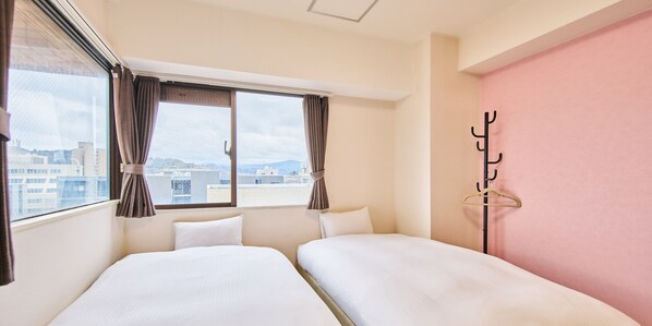 A hotel room with two beds, a window with curtains, a coat rack, and a view of buildings.