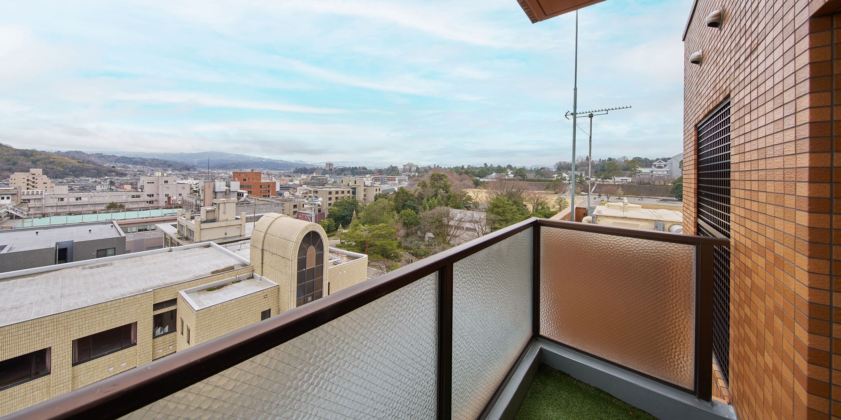Un balcón con vistas a un paisaje urbano, que incluye edificios y una cadena montañosa distante.