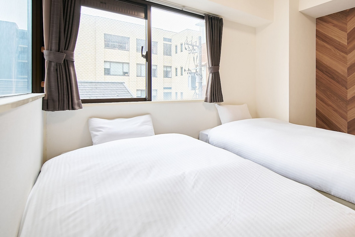 Habitació d'hotel amb dos llits, una finestra amb cortines i un mur amb dibuix de guilló.