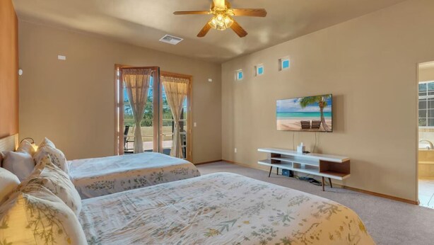 A hotel room with two beds, a ceiling fan, a TV, and a view of the outdoors.