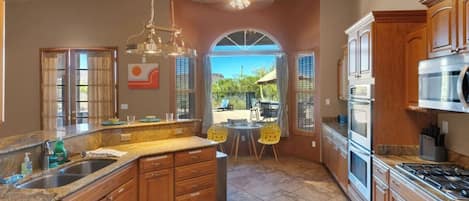 A kitchen with wooden cabinets, a granite countertop, a built-in oven, and a dining area with chairs.