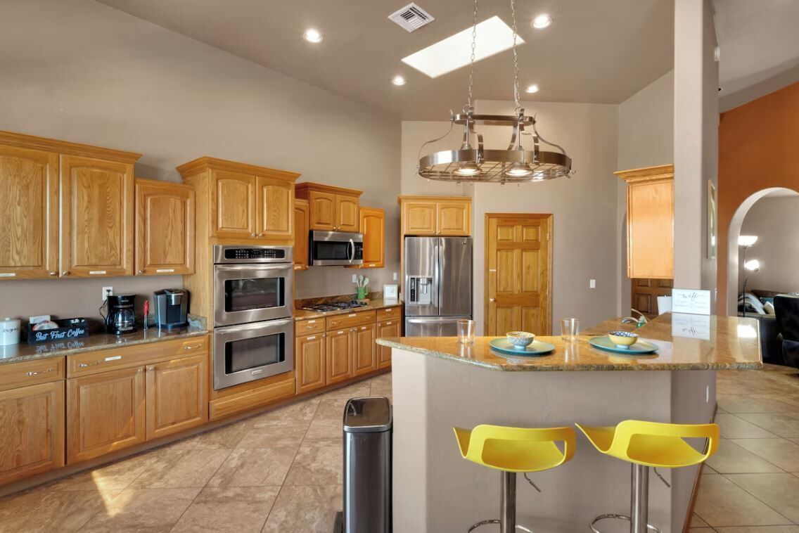 A modern kitchen with wooden cabinets, stainless steel appliances, and a central island with yellow bar stools.
