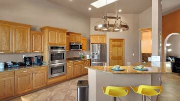 A modern kitchen with wooden cabinets, stainless steel appliances, and a central island with yellow bar stools.