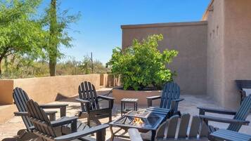 An outdoor patio with Adirondack chairs, a fire pit, and a potted plant.