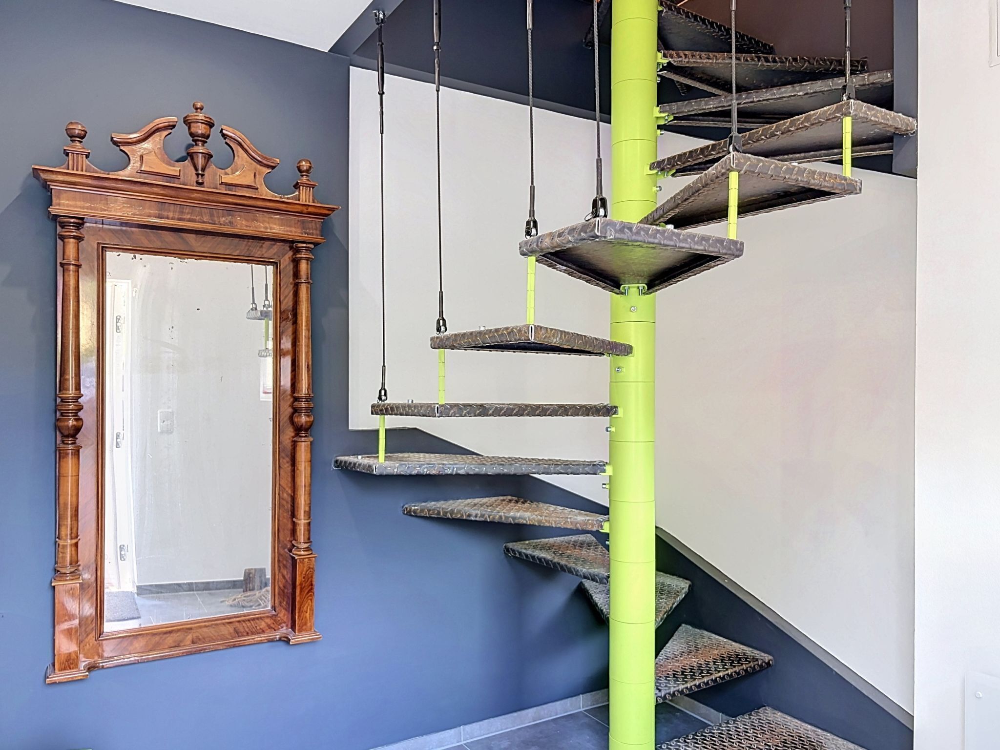 Eine Wendeltreppe mit einem grünen Pfosten und einem rahmenförmigen Spiegel an der Wand.