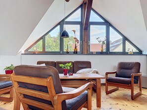 Ein modernes Loft mit schrägverdeckter Decke, Holzmöbeln und großen Fenstern mit Blick ins Freie.