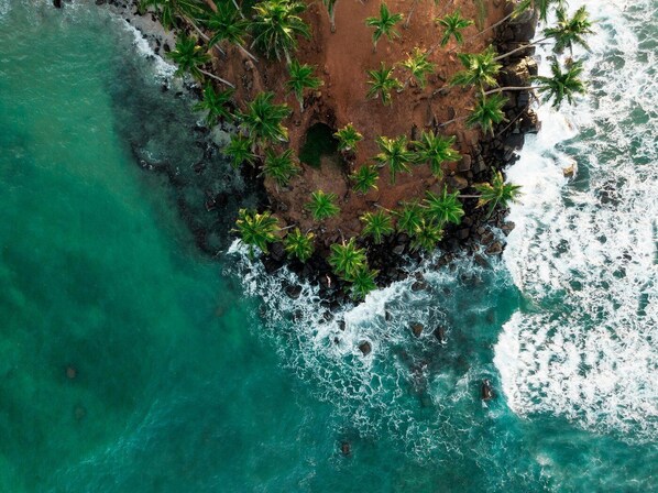 Vista aérea de una isla tropical con aguas turquesas cristalinas, una playa de arena y palmeras.