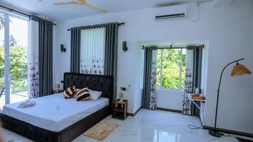 A modern bedroom with a large bed, a ceiling fan, an air conditioning unit, and a view of greenery outside.
