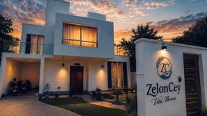 Una villa moderna con una entrada bien iluminada, un camino de acceso y un cartel que indica el nombre 'Zeloncey Villa Mirissa'.