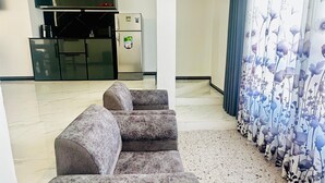 Un espacio de estar con un conjunto de sofás, una cocina con electrodomésticos modernos y una cortina decorativa con estampado floral.