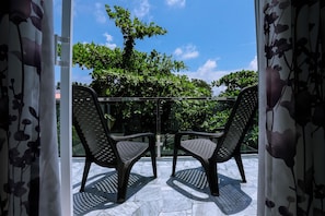 Ein Balkon mit zwei Stühlen und einem Glasgeländer, mit Blick auf einen Garten mit Bäumen und einem klaren Himmel.