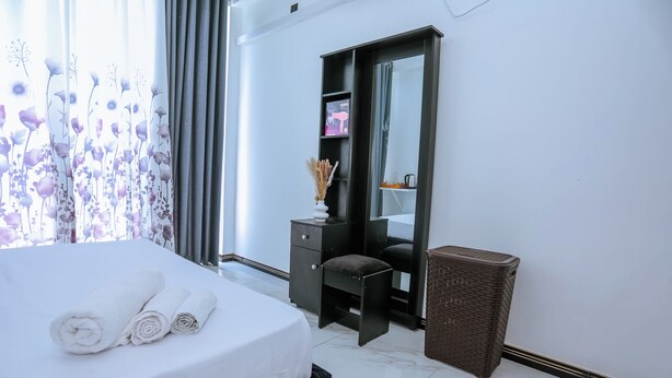Habitación de hotel con cama, escritorio, espejo, basurero y ventana con cortinas.