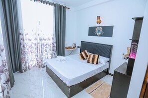 A hotel room with a bed, a bedside table, a wall-mounted artwork, and a window with curtains.
