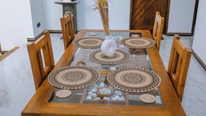 Una mesa de comedor con cubierta de vidrio, rodeada de sillas de madera y decorada con posavasos estampados.