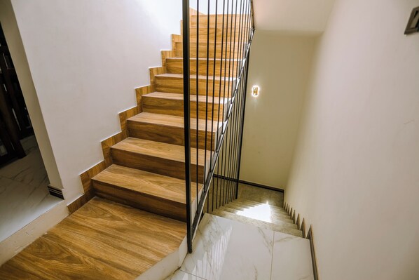 Un escalier avec des marches en bois et une rampe en métal, menant à un palier où se trouve un luminaire.