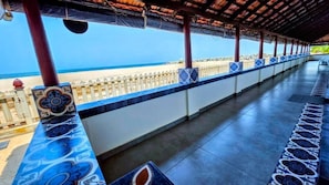 A covered walkway with a view of the beach, featuring a patterned railing and tiled flooring.