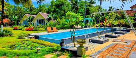 Zona de piscina con una piscina azul cristalina, rodeada de palmeras y un jardín bien cuidado.