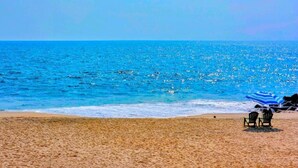 Una spiaggia con acque cristalline, una riva sabbiosa e due sedie sotto un ombrellone a righe.
