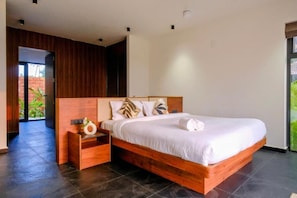 A modern bedroom with a wooden bed frame, a nightstand, and a view of greenery outside.
