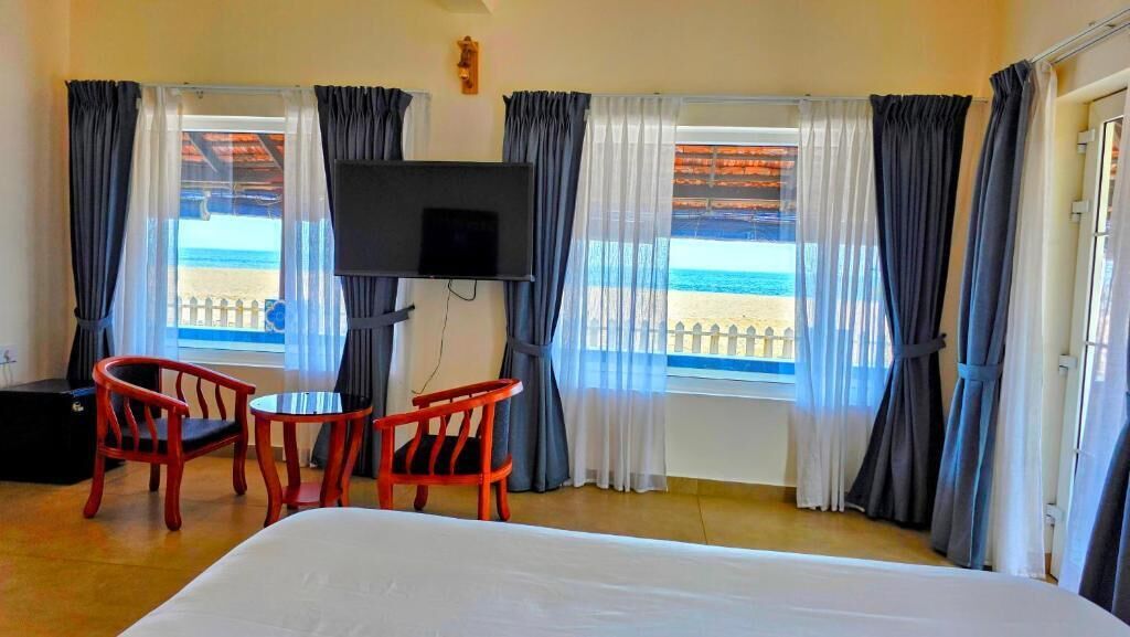 Una habitación de hotel con una cama, dos sillas rojas, un televisor y vista a la playa.