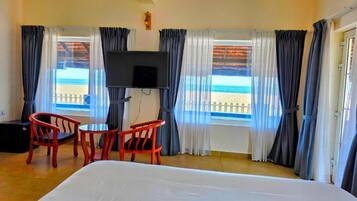 Una habitación de hotel con una cama, dos sillas rojas, un televisor y vista a la playa.