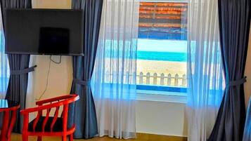 Una habitación con una cama, un televisor montado en la pared, una ventana con vista a la playa y una silla roja.