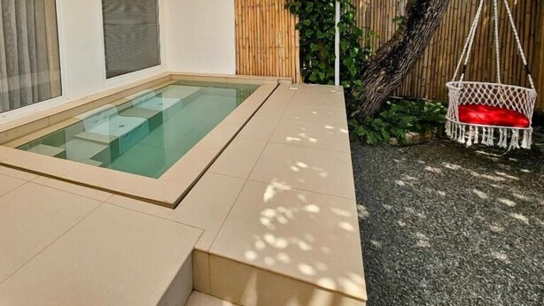Area piscina con recinto in vetro, una sedia a dondolo e una recinzione in legno.