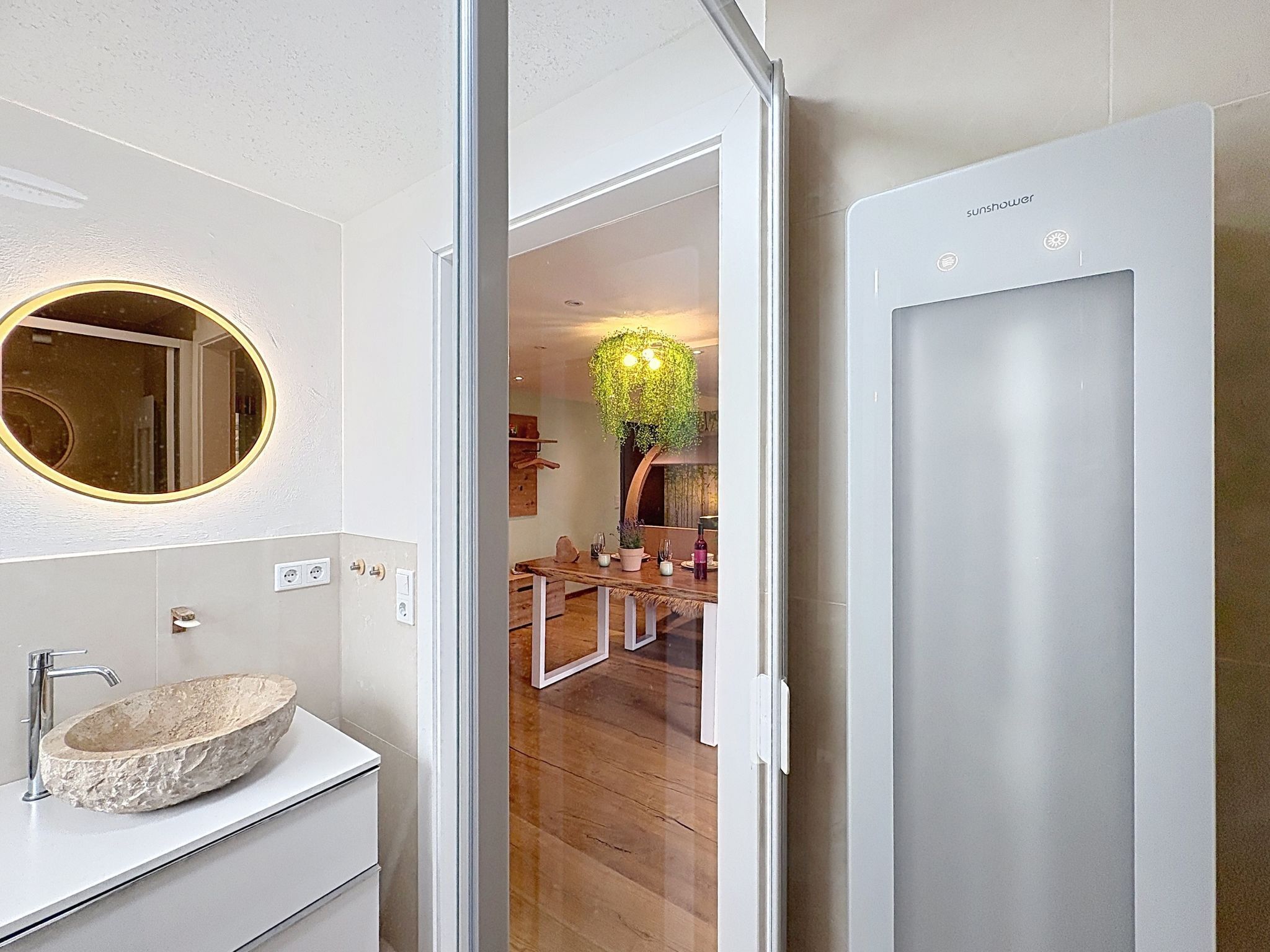 Un baño moderno con un lavamanos de piedra, un espejo redondo con marco dorado y una puerta blanca.