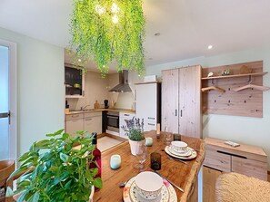 Eine moderne Küche mit Holzschränken, einer hängenden Pflanze und einem Esstisch, gedeckt mit Tellern und einer Vase.