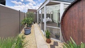 Eine moderne Terrasse mit Glasveranda, Topfpflanzen und Holzlattenzaun.