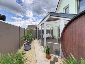 Eine moderne Terrasse mit Glasveranda, Topfpflanzen und Holzlattenzaun.
