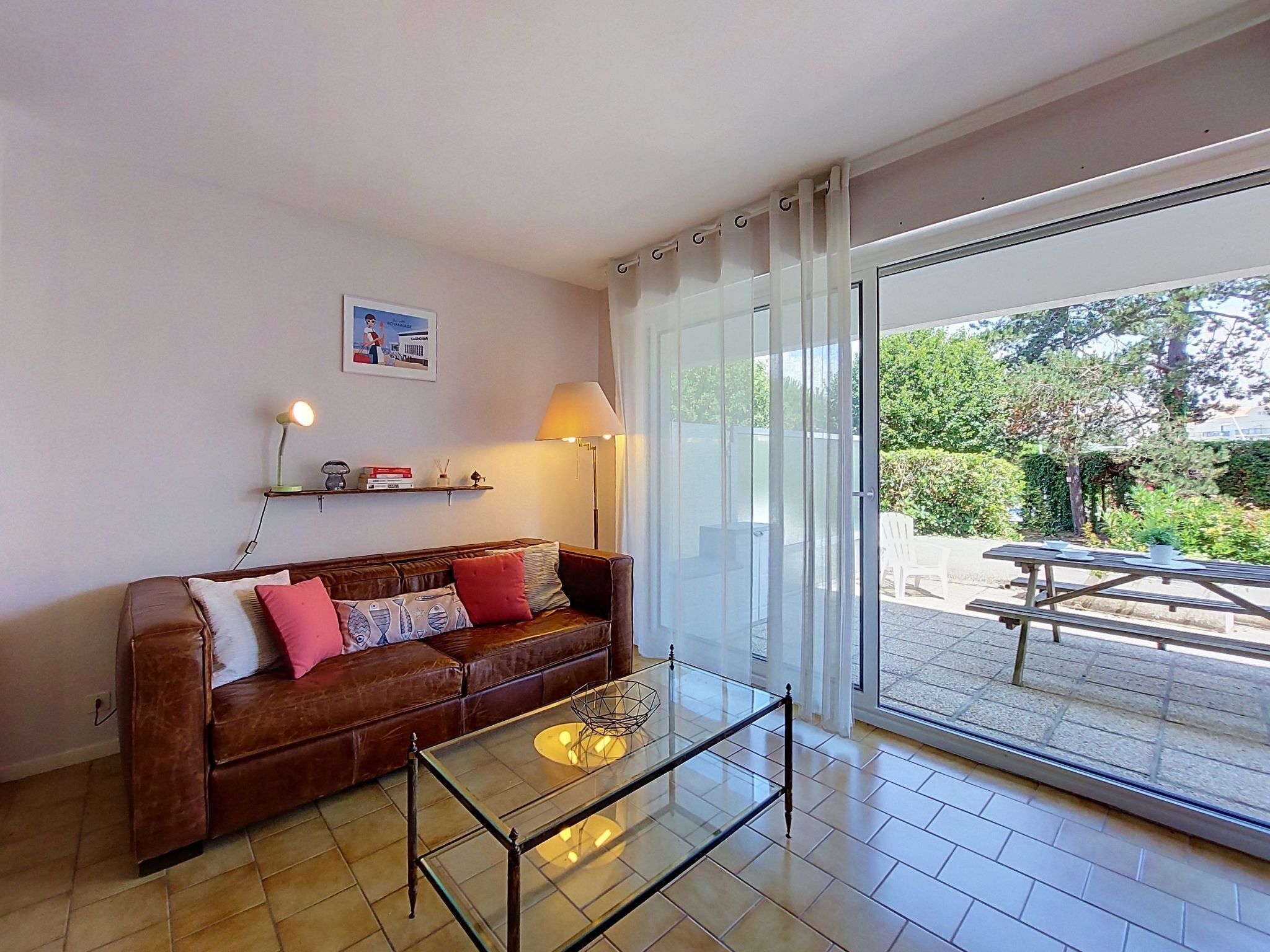 A living room with a brown leather sofa, a glass coffee table, and a sliding glass door leading to an outdoor patio.
