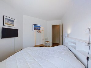 A bedroom with a bed, a television, a chair, a wooden ladder, and a door leading to another room. - La Frégate by Interhome (Vaux Sur Mer)